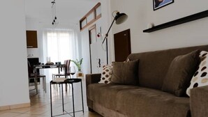 Uma sala de estar com um sofá marrom, uma mesa de centro e uma área de jantar ao fundo.