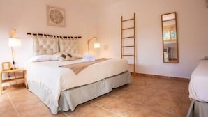 A bedroom with a large bed, two bedside lamps, a ladder, and a mirror on the wall.