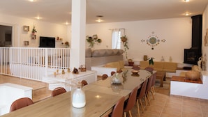 A modern living room with a glass dining table, beige sofa, and a TV mounted on the wall.