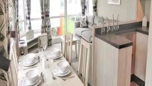A dining area with a table set for four, a sofa, and a kitchen island with a sink. - Luxury 2 Bed Caravan Heacham Beach Pets go Free (King's Lynn)