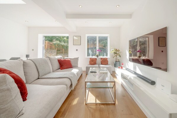 Ein modernes Wohnzimmer mit einer Couch, einem Hocker, einem Glastisch und einem flachbildfernseher an der Wand.