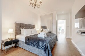 Ein Schlafzimmer mit einem großen Bett, einem Nachttisch, einer Lampe, einem Spiegel und einer Chandelier.