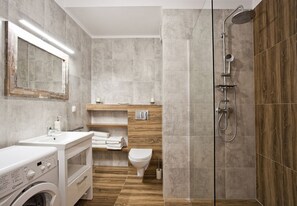 Bathroom features a washing machine, toilet, and shower area with a glass-enclosed shower.