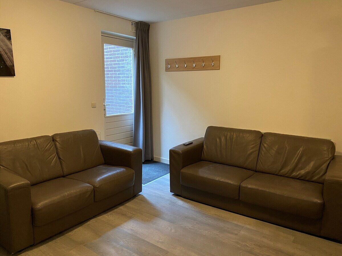 Ein Zimmer mit zwei braunen Ledersofas, einem Holz-Kleiderständer und einer Tür, die auf einen Balkon führt.