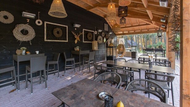 An outdoor dining area with wicker furniture, hanging lights, and decorative wreaths on the walls.