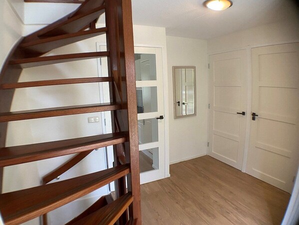 Un escalier menant à une pièce dotée d’une porte blanche, d’un miroir et d’une armoire à deux portes.