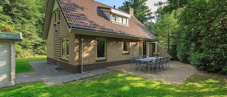 Una casa de un piso con techo inclinado, un pequeño garaje adosado y un patio con mobiliario exterior.