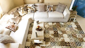 Un salon avec un canapé beige, des coussins à motifs, une table basse ornée d’un plateau décoratif et un sol carrelé présentant différents motifs géométriques.