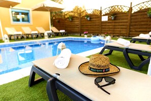 A poolside area with lounge chairs, a sun umbrella, and a hat with "Greece Rhodes" written on it.