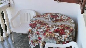 A small balcony with a round table covered with a floral tablecloth, two white plastic chairs, and a patterned cushion. - Apartment for a Single Person (Komiza)