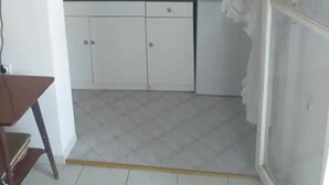 A small kitchen with white cabinets, a countertop, and a sink. There is a chair and a table in the corner. - Apartment for a Single Person (Komiza)
