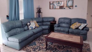 A living room with a sectional sofa, a coffee table, a ceiling fan, and a wall art piece.