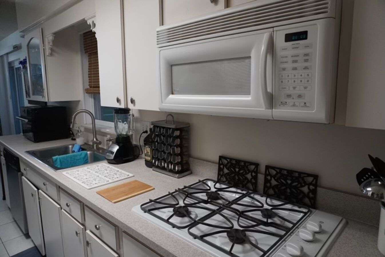 Une cuisine équipée d’une cuisinière à gaz, d’un four à micro-ondes, d’un évier, d’un mixeur et d’un bloc à couteaux.