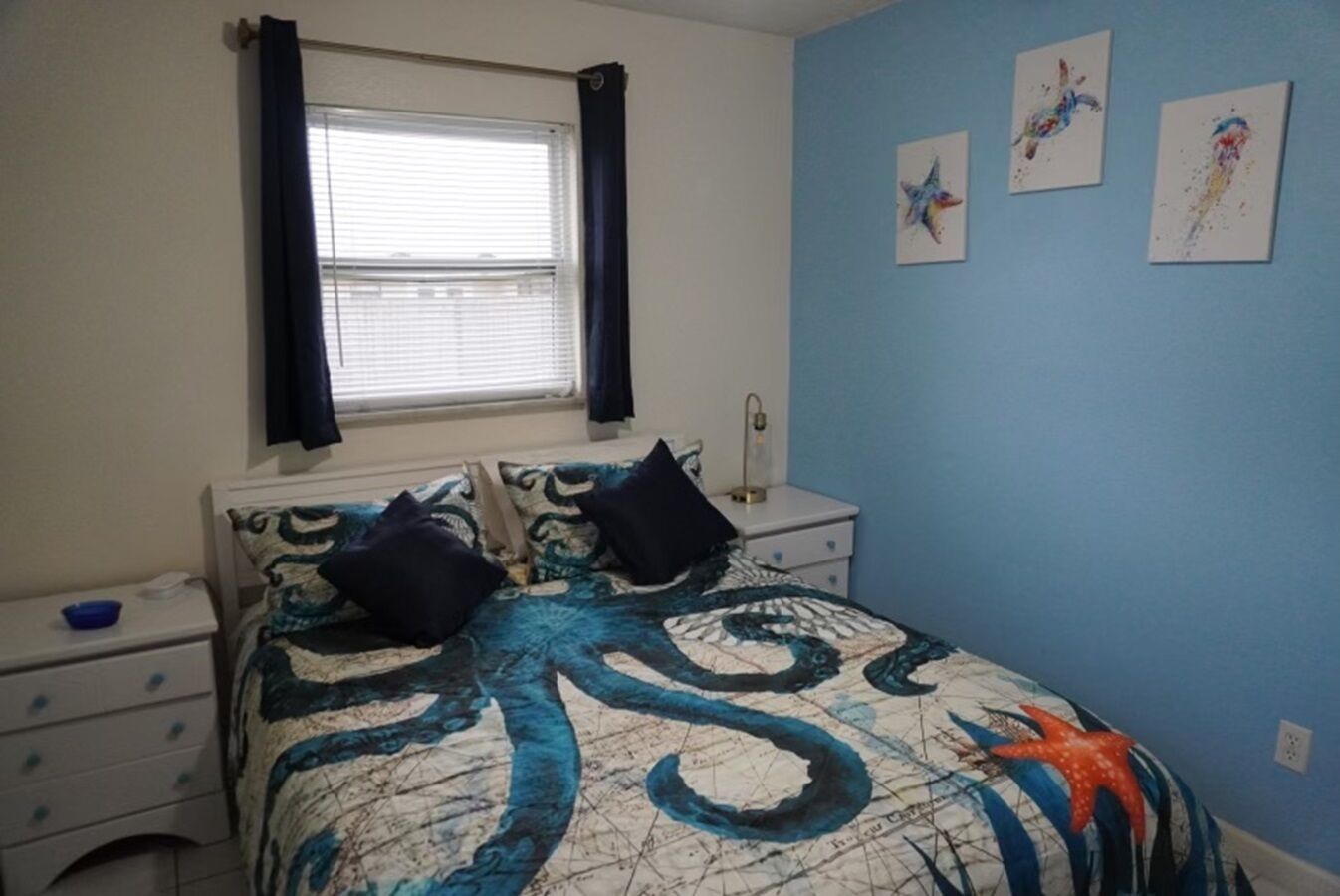 Een slaapkamer met een bed, nachtkastje, raam met gordijnen en decoratie aan de muur.