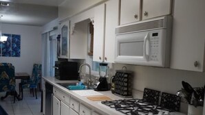 A kitchen with white cabinets, a microwave, a gas stove, and a blender. There is a blue rug on the floor.