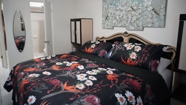 A bedroom with a bed, a mirror, a wardrobe, and a floral artwork on the wall.