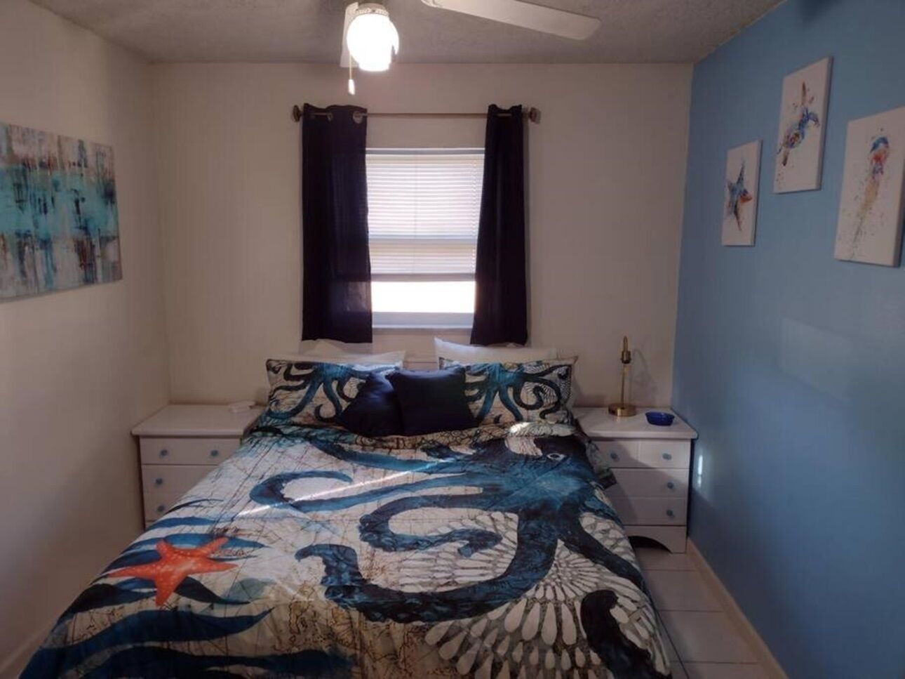 Ein Schlafzimmer mit einem Bett, zwei Nachttischen, einem Fenster mit Vorhängen und Wandbildern.