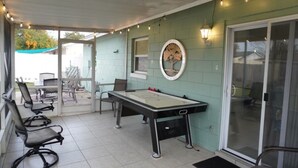 A covered patio area with a foosball table, chairs, and a dining table.