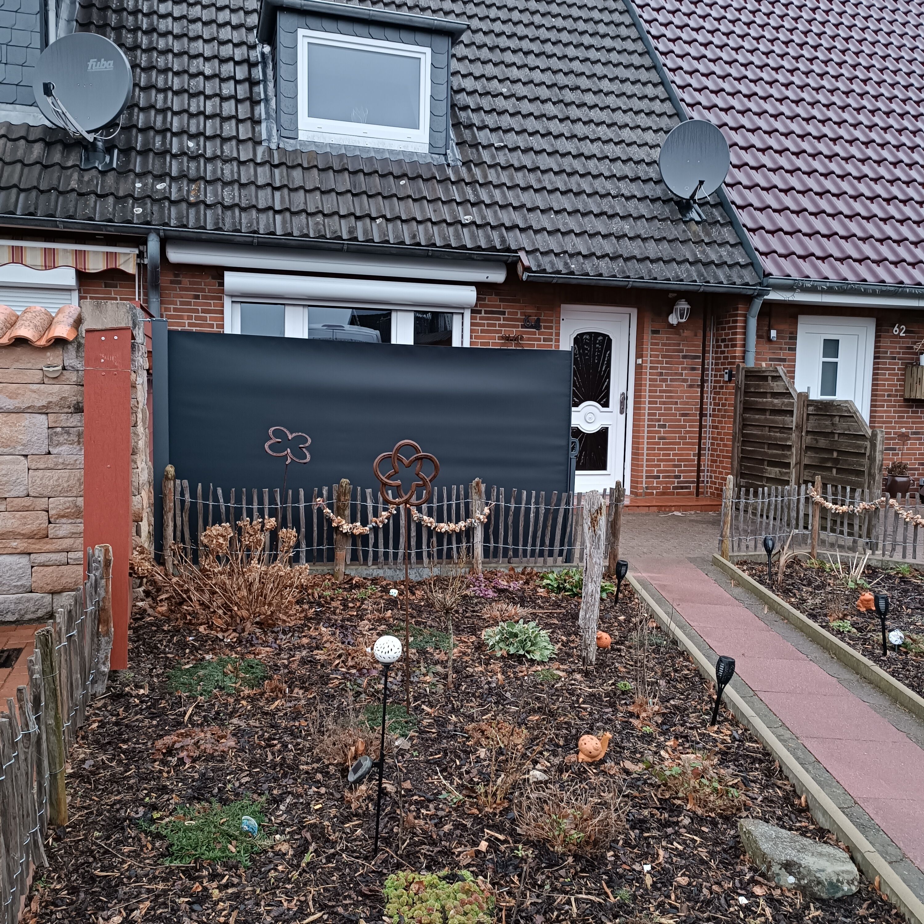 Una casa residencial con techo de tejas, antenas parabólicas, fachada de ladrillo y jardín con acolchado vegetal y plantas.