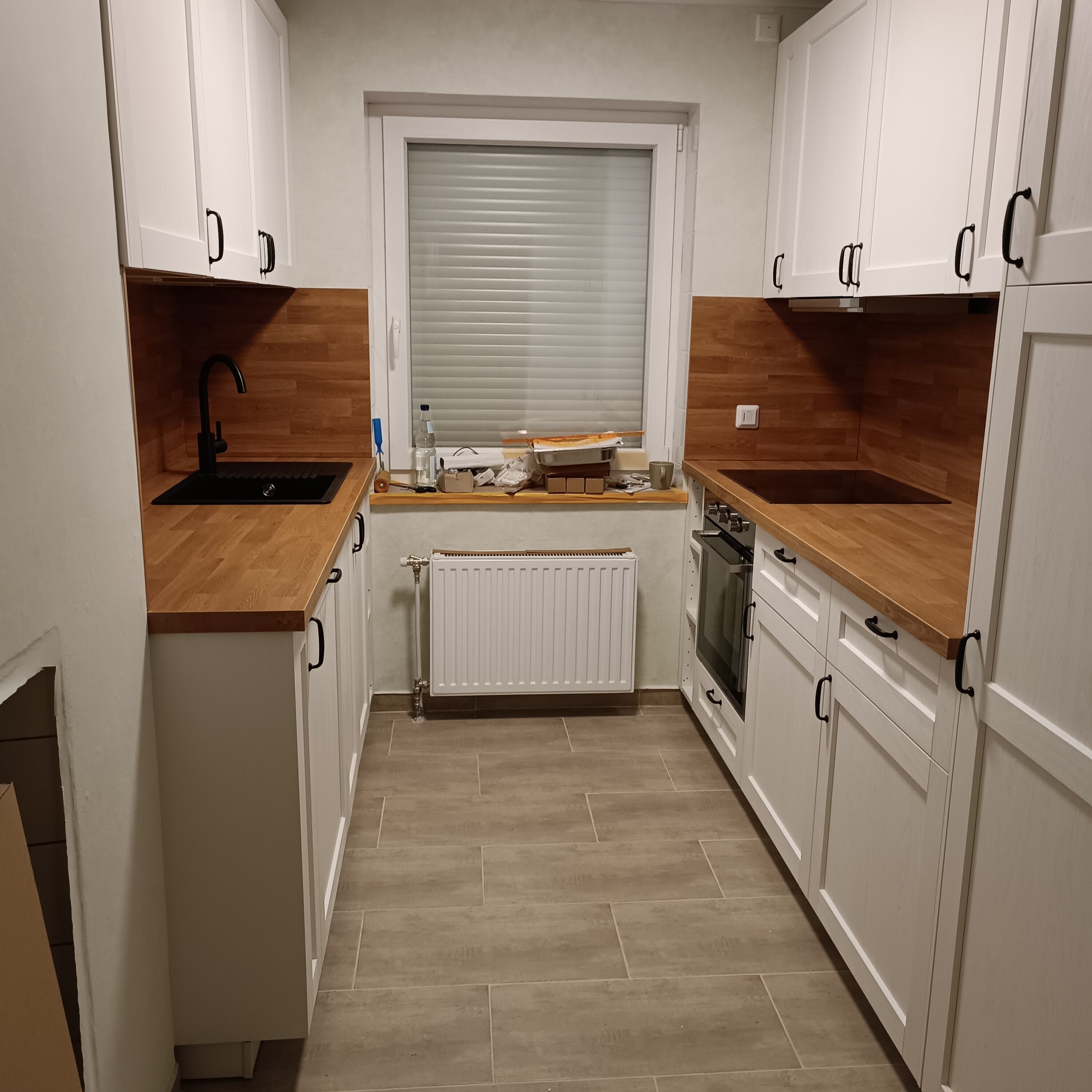 A compact kitchen with white cabinets, wooden countertops, a built-in oven, and a window with blinds.