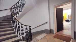 A staircase with ornate black railings leading to a room with a tiled floor and a door leading to another room. - Yellow Palm - 60m2 - cozy, central with a green view (Wien)