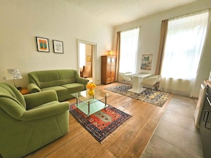 A living room with a green sofa, a glass coffee table, and a patterned rug.