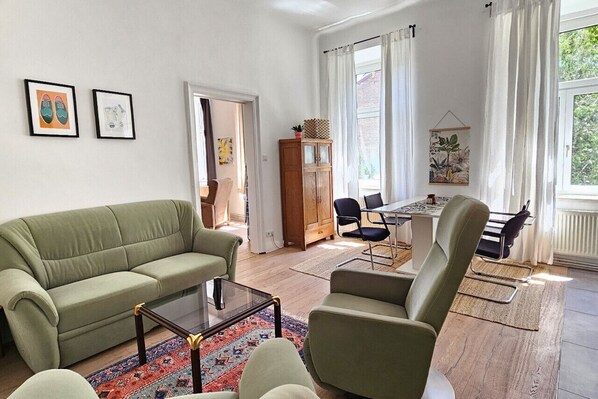Een woonkamer met een groene bank, een glazen salontafel, en een eethoek met een tafel en stoelen.