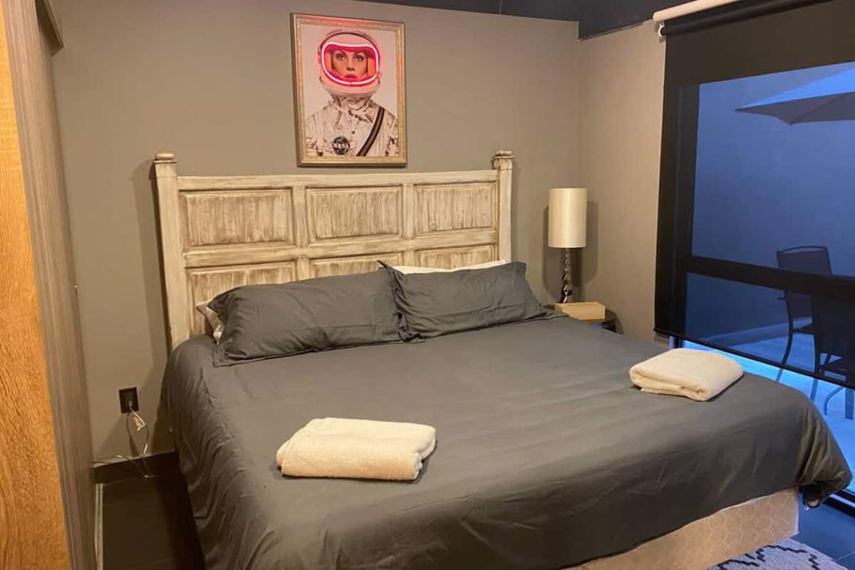 A hotel room with a large bed, a headboard, a nightstand, a lamp, and a view of the outside.