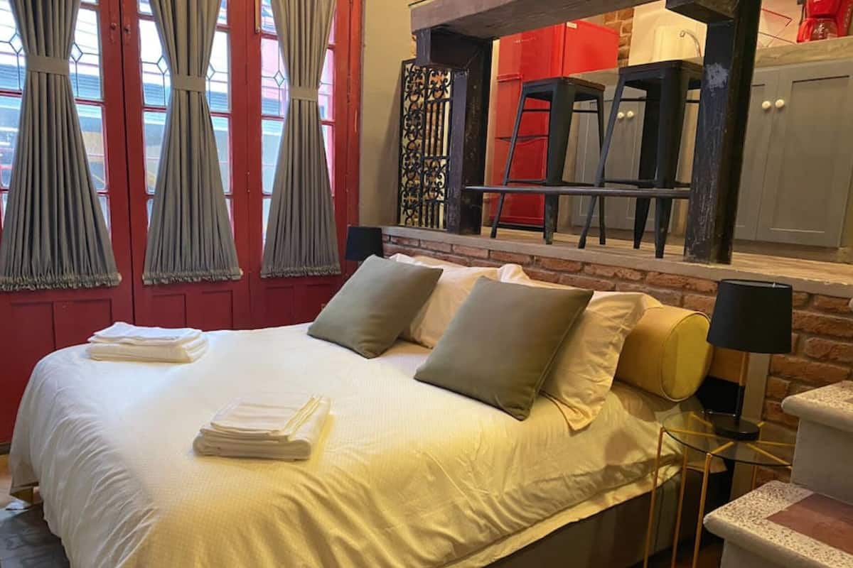 A neatly made bed with pillows and folded towels, a brick wall, and a red cabinet in the background.