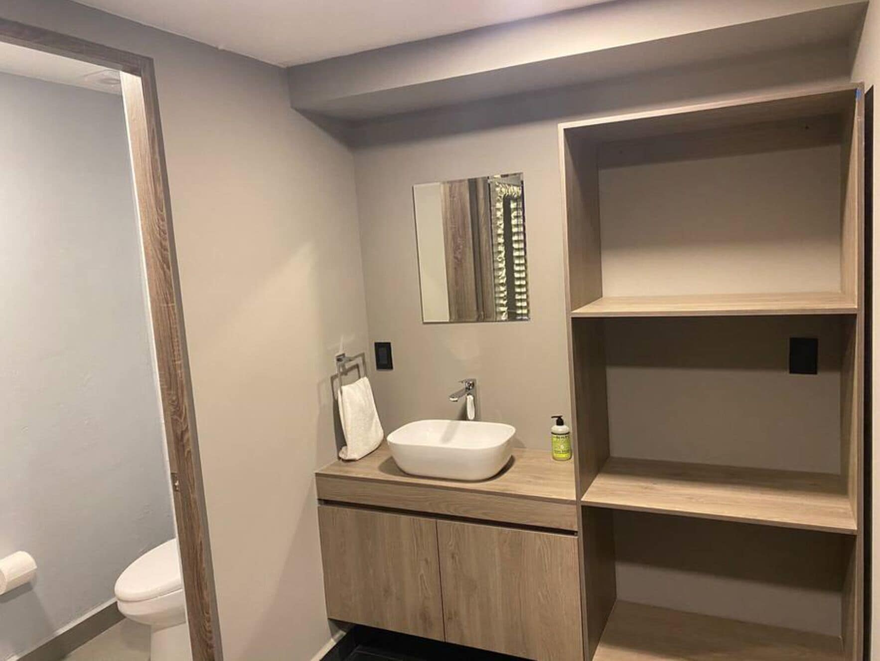Een moderne badkamer met een witte wastafel, een houten opbergmeubel en een spiegel.