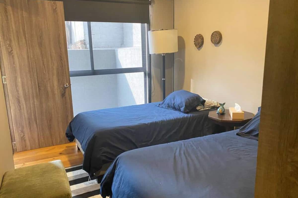 A room with two beds, a wooden door, a lamp, and a small table with a tissue box.