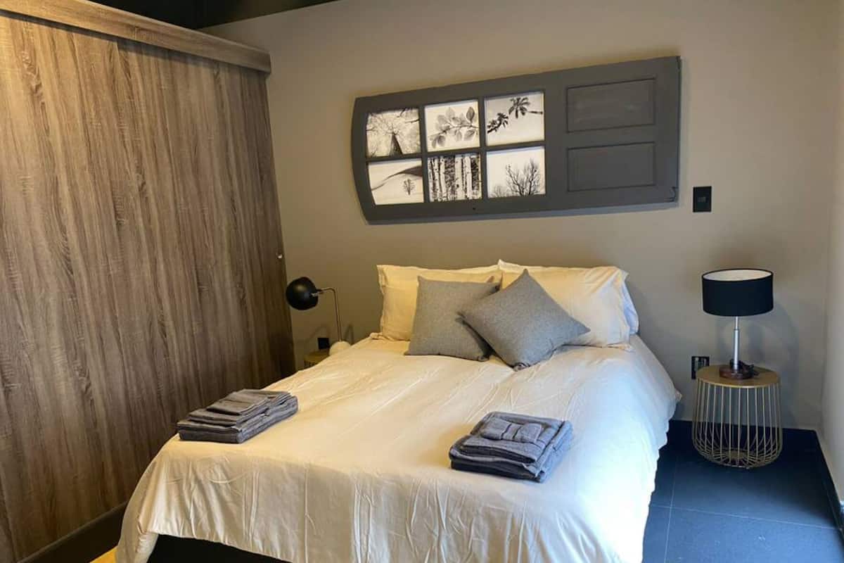 A neatly made bed with pillows and folded towels, a bedside lamp, and a wall-mounted artwork above the bed.
