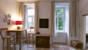 A room with a wooden table, two chairs, a small cabinet, a radiator, and a window with curtains.