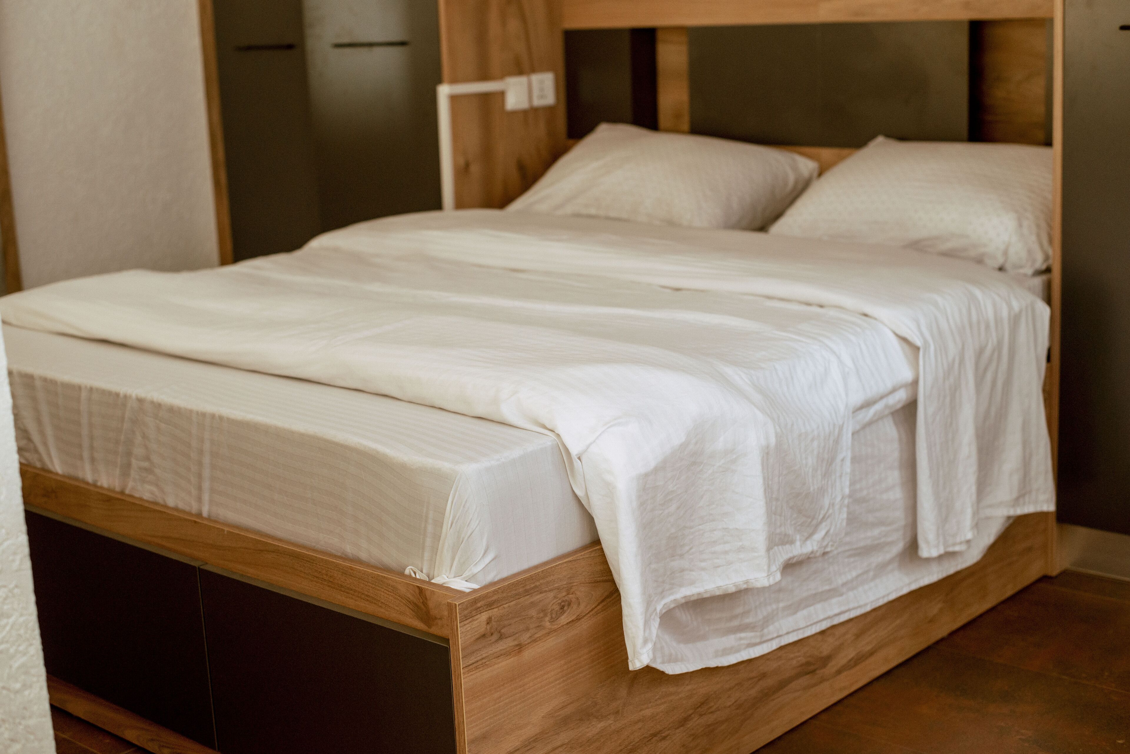 A wooden bed with white bedding in a room with a wooden floor and a wooden headboard.