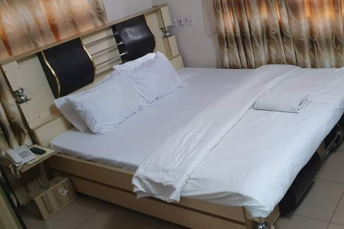Cama bem arrumada com lençóis brancos, cabeceira de madeira e mesa de cabeceira com um telefone.