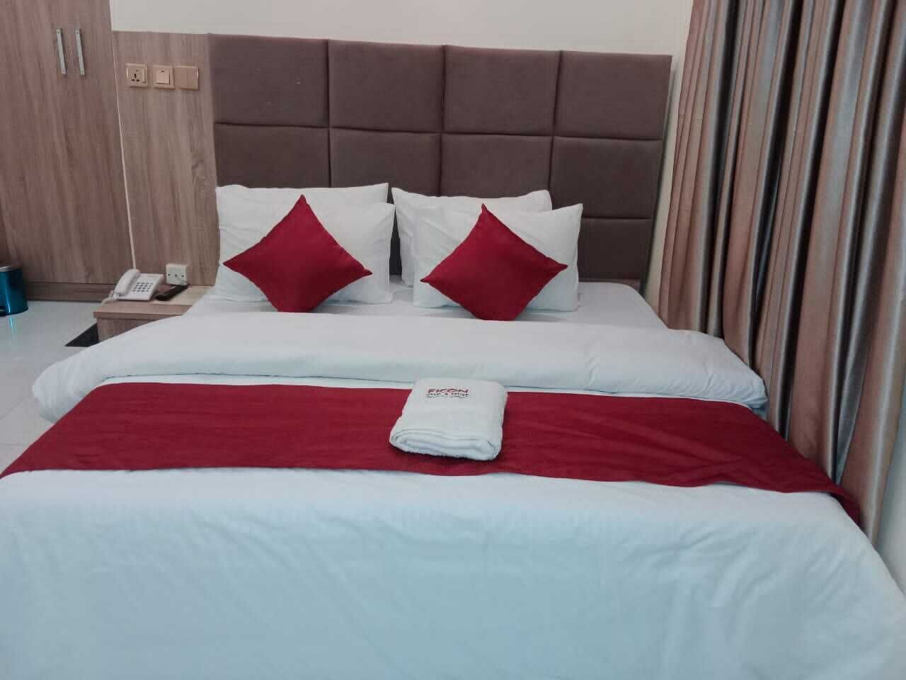 Una cama bien hecha con ropa de cama blanca y roja, un cabecero marrón y una manta roja.