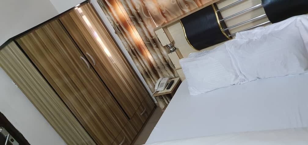 Une chambre avec une armoire en bois, un lit avec une literie blanche et un téléphone sur une table de chevet.