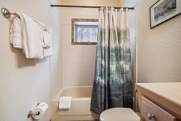 A bathroom with a bathtub, a toilet, and a shower curtain with a forest design. - Lupine Chalet - Frisco Ski Home, New Hot Tub, Fireplace, Near 3 Resorts, Sleeps 10 (Frisco)