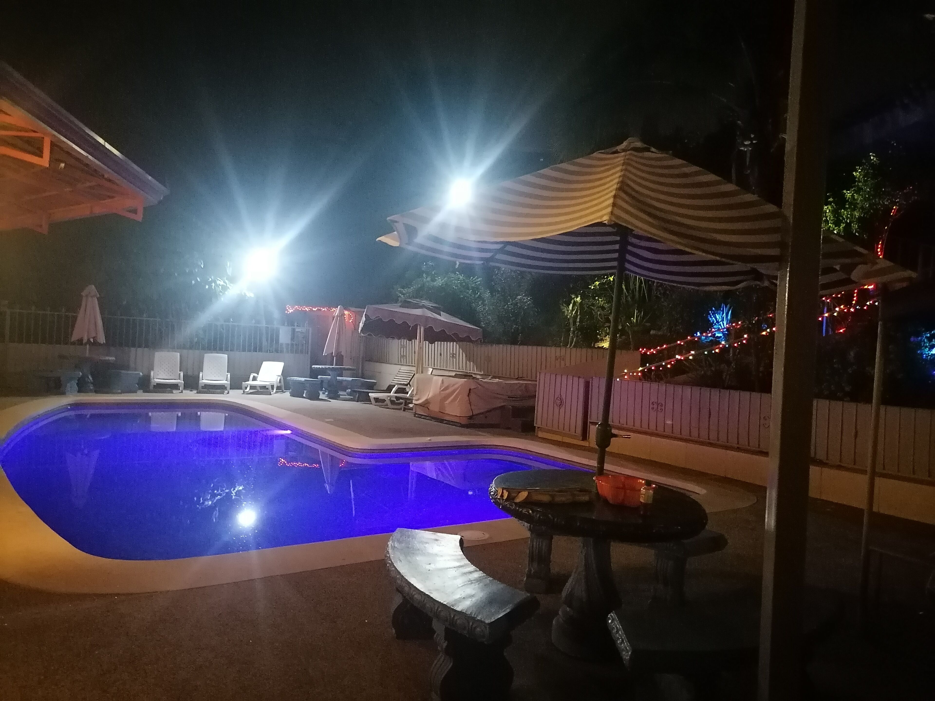 Una piscina amb gandules i una ombra, envoltada per una tanca de fusta i llums de cadena.