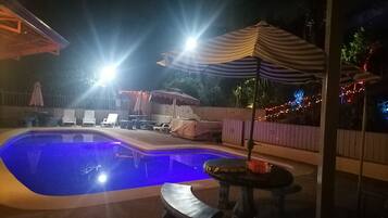 Una piscina amb gandules i una ombra, envoltada per una tanca de fusta i llums de cadena.