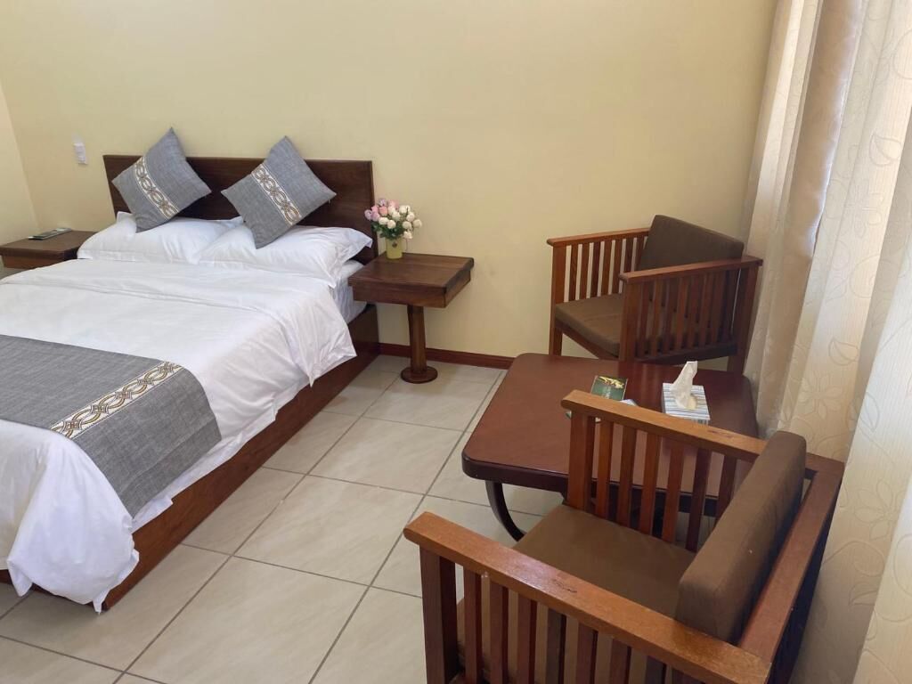 A hotel room with a bed, a wooden chair, a small table, and a nightstand.