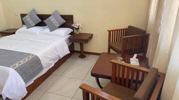 A hotel room with a bed, a wooden chair, a small table, and a nightstand.