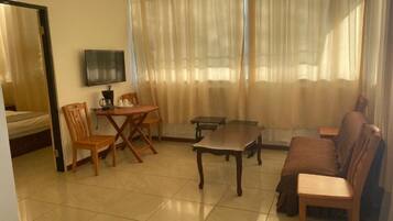 A living room with a sofa, two chairs, a coffee table, a TV, and a dining table.
