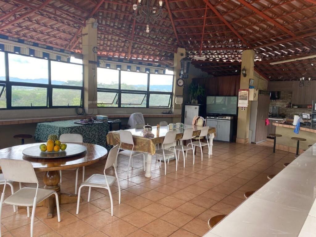 A spacious dining area with a round table and chairs, a kitchen area with a TV, and large windows offering a view of the landscape.