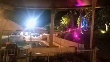 A covered outdoor area with a pool, lounge chairs, and string lights.