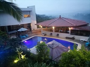 A swimming pool with lounge chairs and umbrellas, a covered patio area, and a view of the surrounding landscape. - Villa garita inn (La Garita)