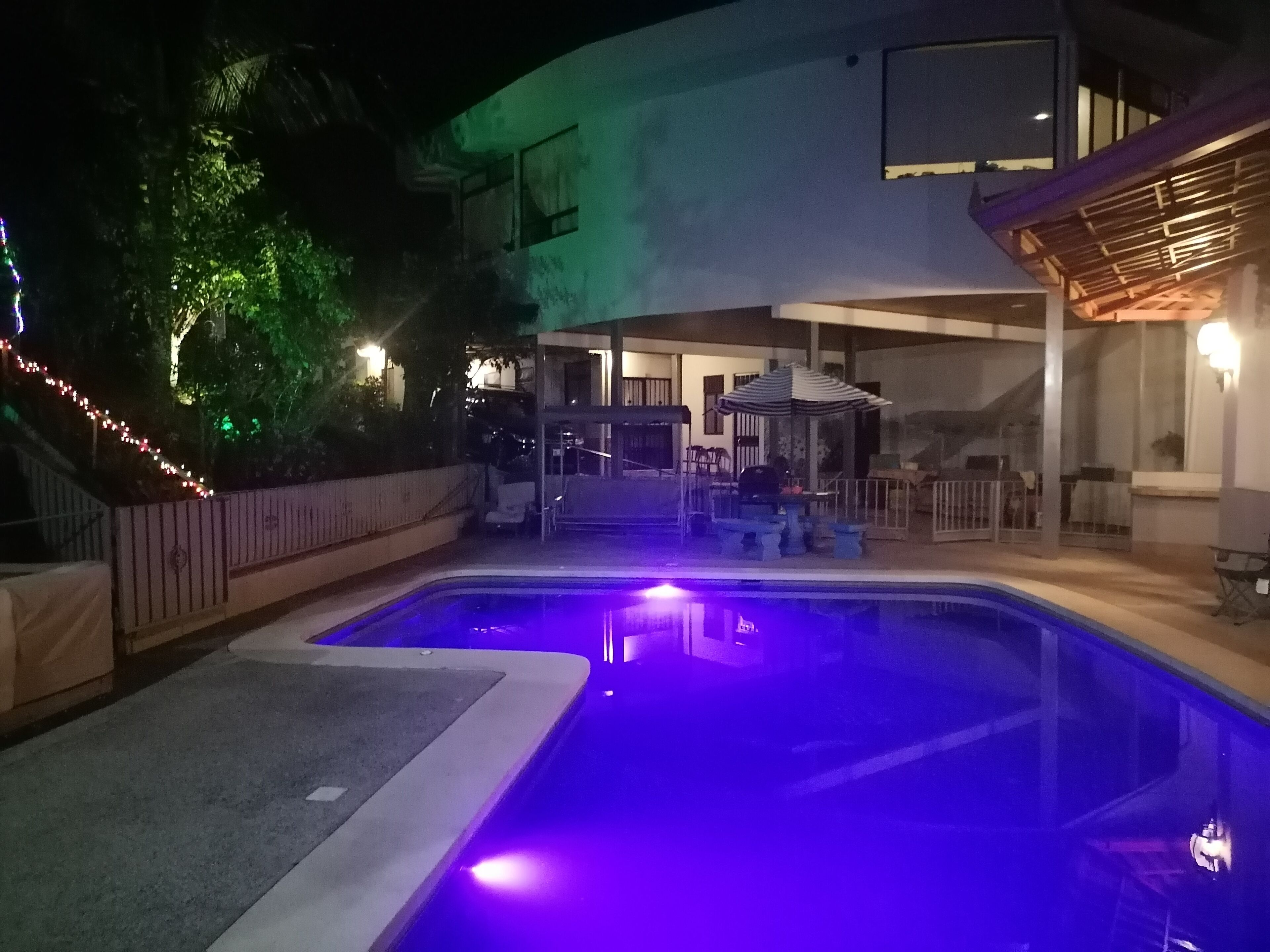 Une piscine avec un espace patio, un coin salon couvert et un bâtiment doté d’un balcon.