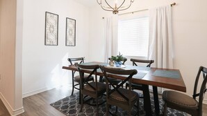 Un'area pranzo con un tavolo rettangolare, sei sedie, un lampadario e due opere d'arte astratte appese alle pareti.
