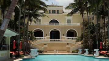 Un resort con una gran piscina, palmeras y un edificio con ventanas arqueadas y un balcón.