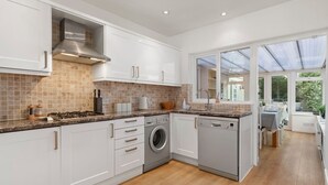 A modern kitchen with white cabinetry, a built-in washer and dryer, and a large window providing natural light. - Kittiwake - Short Walk to Beach and Village (Saundersfoot)